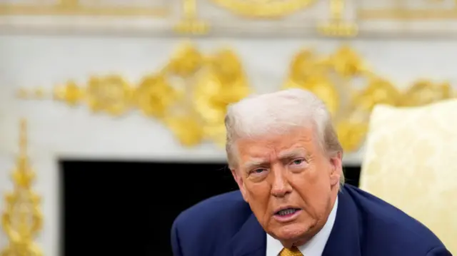 Trump in blue suit with gold tie in front of gold and white fireplace