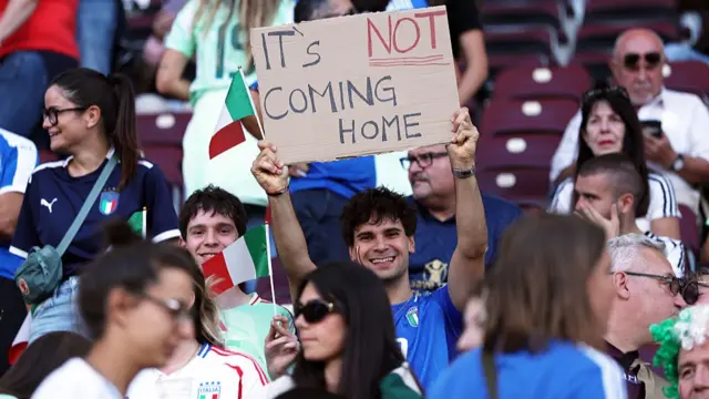 Fans of Italy hold up a sign saying "it's not coming home"