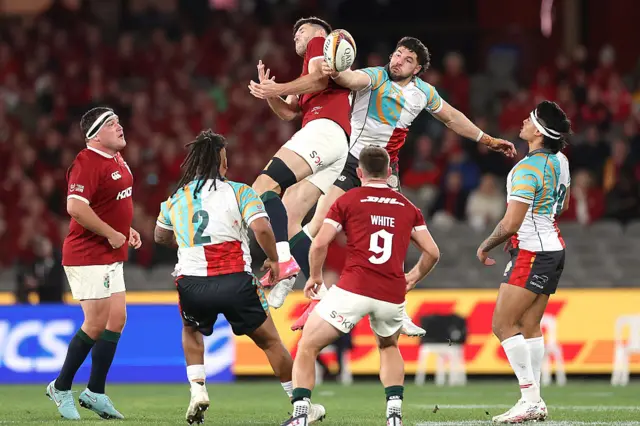 British and Irish Lions' Blair Kinghorn (C) and First Nations & Pasifika XV' Filipo Daugunu compete for a high ball
