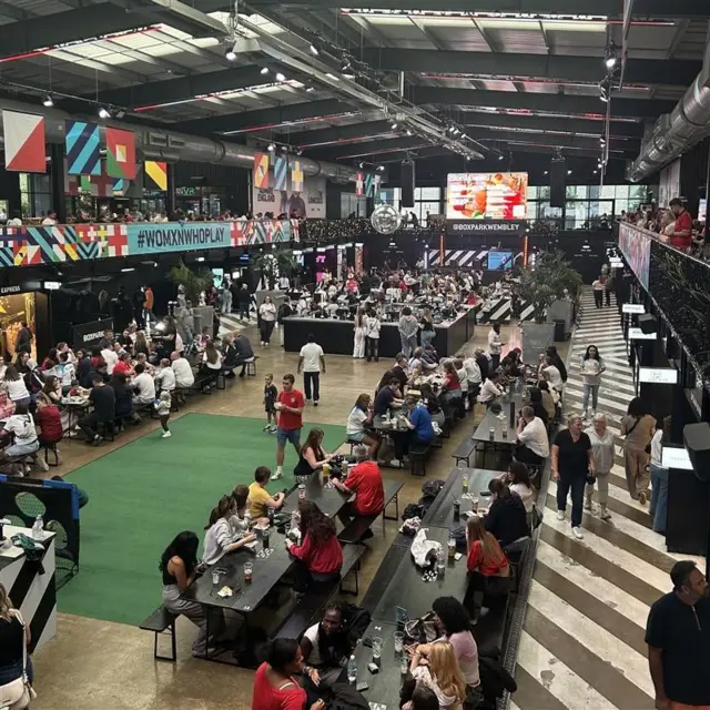 Fans sitting  on long tables at Boxpark Wembley
