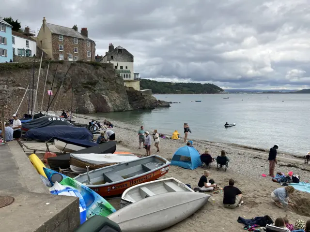 People and boats sit on the sands at the beach in Cawsands.