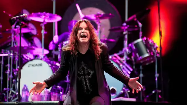 Ozzy Osbourne has his hands wide to his sides and opening his mouth wide as he sings