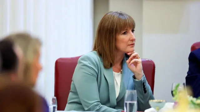 Chancellor Rachel Reeves at the Mansion House dinner, resting her chin on two fingers. She is wearing a light blue jacket and sitting in a red leather chair.