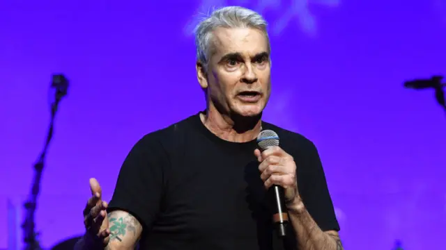 Henry Rollins, holding a microphone in his left hand, performs onstage