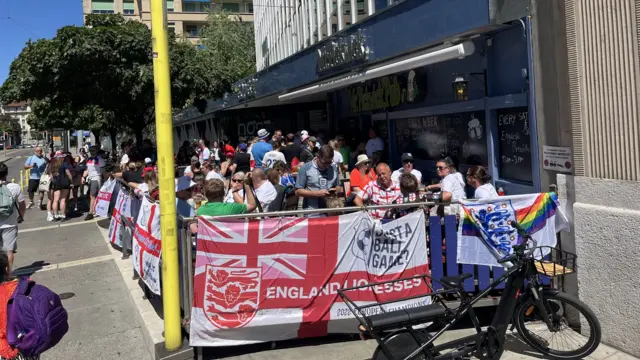 England supporters sit next to an 'England Lionesses' flag in Geneva