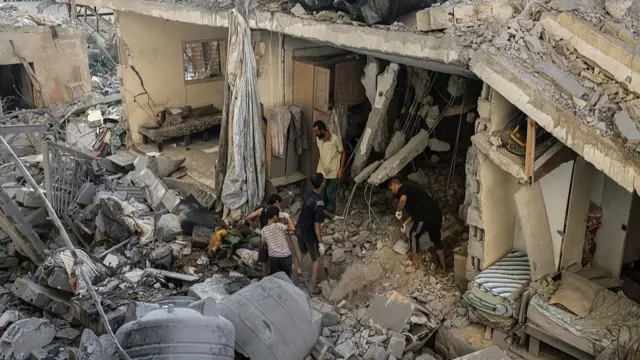 A birds eye view of damaged buildings that have been ruined. There is concrete everywhere and men and boys assess the damage