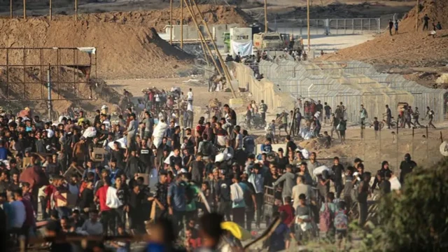 A crowd of people stand near a fenced-off zone which appears to be the aid point