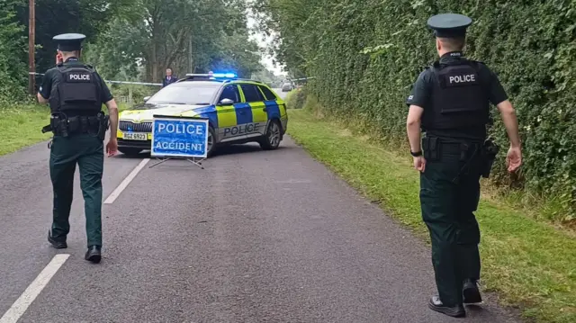 Two uniformed police officers walk towards a yellow and blue branded police car.