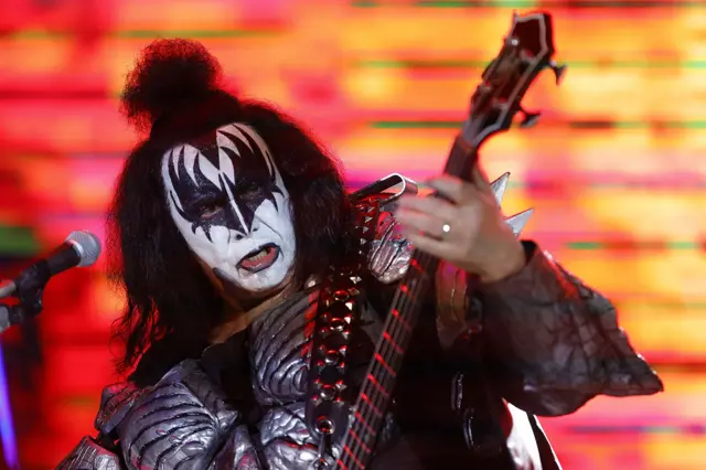Gene Simmons in black and white face paint plays the guitar on stage.
