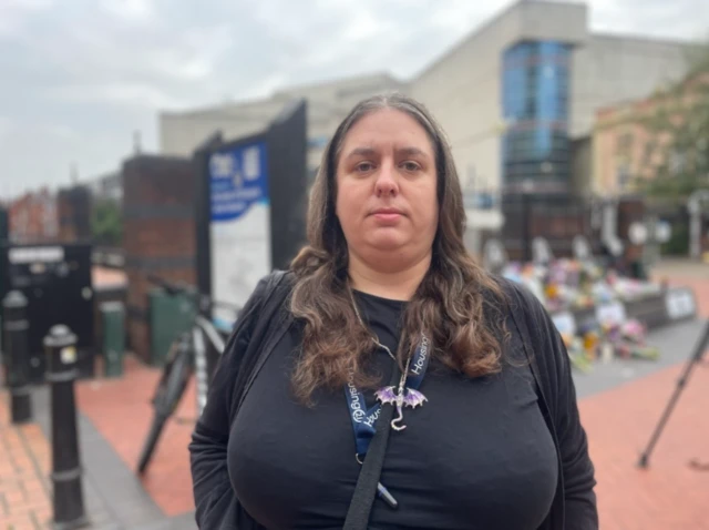 Louise pictured at an Ozzy Osbourne memorial. She has long, brown hair and is dressed in all black clothing with a purple dragon necklace.