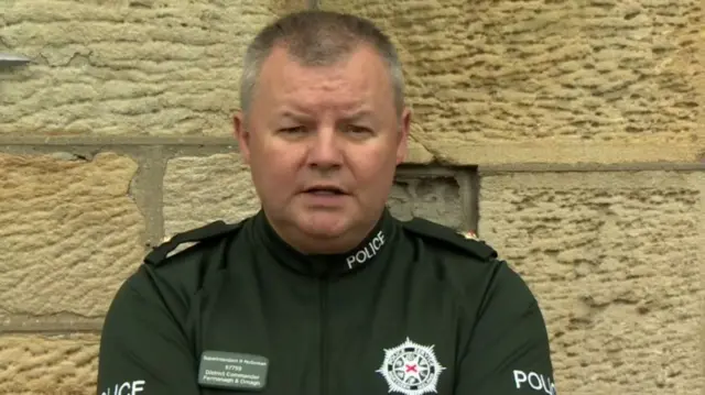 A police officer with short grey and dark hair is wearing a bottle green uniform as he speaks at a press conference.