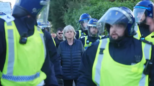 Police officers wearing hi-vis jackets and helmets surround people walking near the hotel.