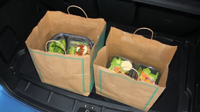 Boxes of food are seen in two brown paper bags in the boot of a car
