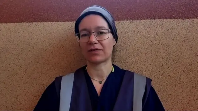 Dr Deirdre Nunan in a blue scrubs and cap leans against an orange and red wall