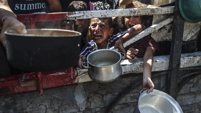 A child in tears holds out a small metal pot as other children also crying hold out pots and pans to collect aid
