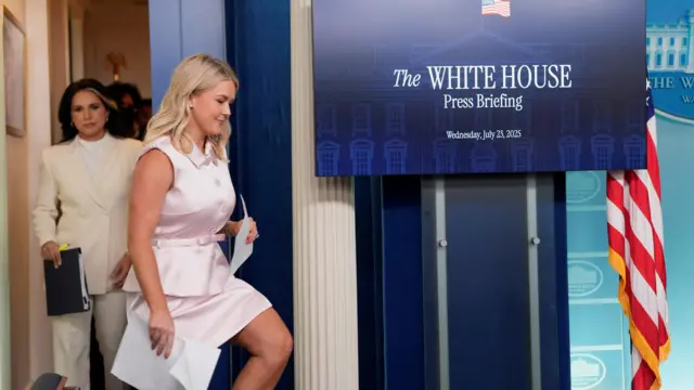 Karoline Leavitt wears a light pink dress and walks towards a podium