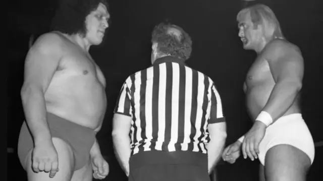 Hulk Hogan stands facing Andre the Giant with a referee in the middle