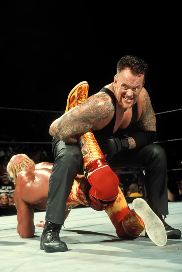 The Undertaker in action against Hulk Hogan during Judgment Day. Hogan is on the ground and the Undertaker is holding his leg, preventing him from getting up.