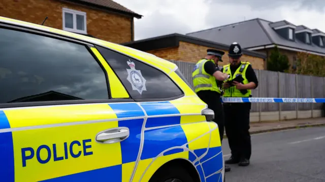 Two police officers stand beside a police car in the middle of a residential street.