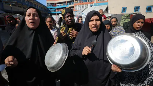 Women holding large bowls and spoons in a crowd.