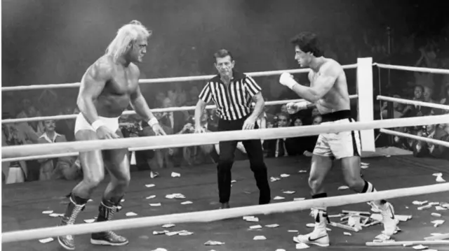 Hogan and Stallone circling each other in a wrestling ring on the set of Rocky III