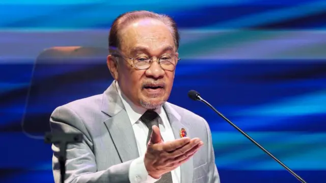 Anwar Ibrahim speaking into a microphone in front of a blue background