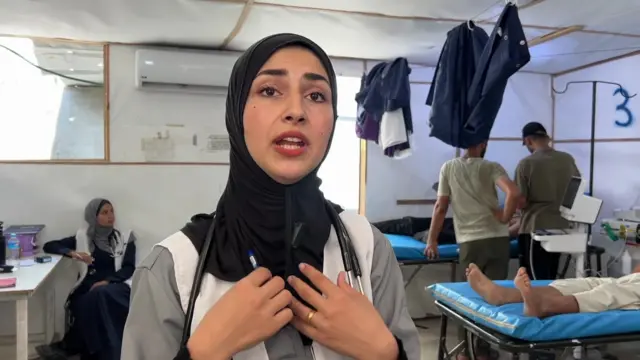 Dr Aseel speaks to an interviewer behind a camera, while people lie in beds behind her