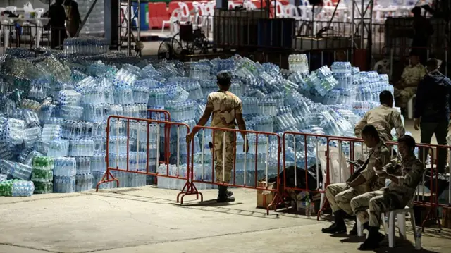 Thai military personnel stands guard over water supplies for people evacuated from border areas