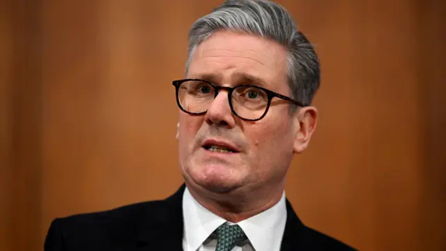 Keir Starmer delivers a statement. He's wearing black rimmed glasses, a black suit and a green-and-blue patterned tie