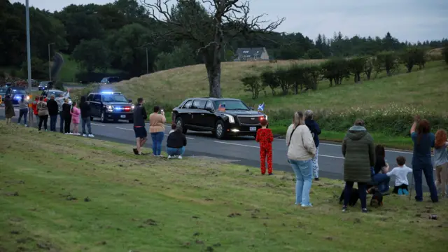 People line the sides of the motorway to watch President Trump pass