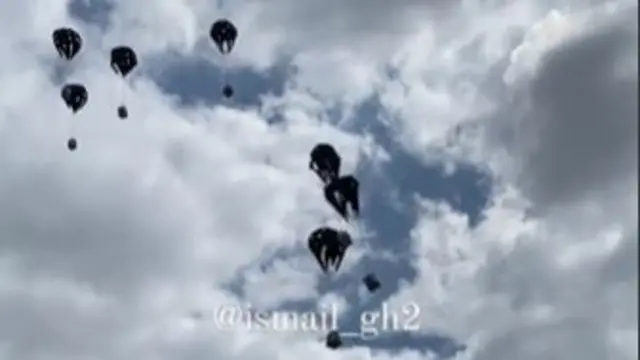 Seven parachutes carrying aid coming down in an air drop. The watermark reads @ismail_gh2