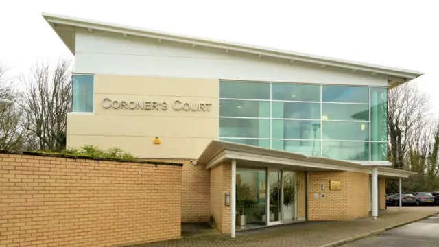 The exterior of Preston Coroner's Court, which is a modern glass and brick building with a slanted roof.