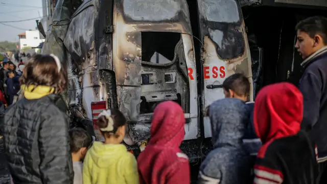 Gazans stand outside a burnt-out van, with lettering indicating it was used by the press