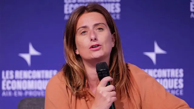 Marine Tondelier in an orange blouse speaks into a microphone
