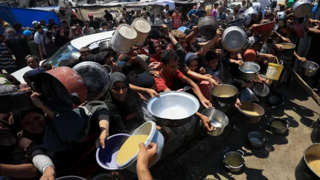 People in Gaza City hold pots and pans to collect aid