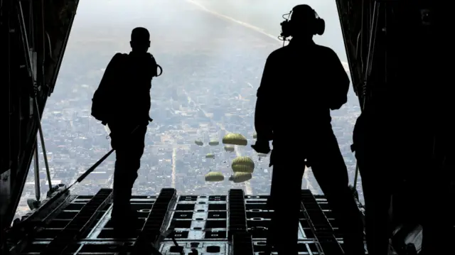 Silhouettes of air force members watch parachutes of aid drop over Gaza