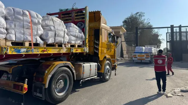 Members of the Egyptian Red Cross look on as trucks loaded with humanitarian aid cross the Rafah border gate
