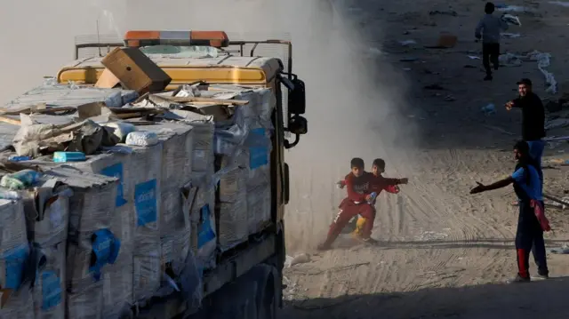 Palestinian children rush to get out of the way of a moving aid truck as they collect aid fallen onto the road,