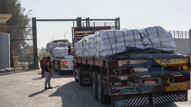 Five man stand next to two lorries carrying aid into Gaza as the vehicles cross through the Egyptian side of the Rafah crossing to the south of the Gaza Strip