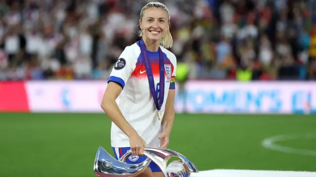 Leah Williamson of England carries the UEFA Women's EURO trophy to the winner's podium after the team's victory
