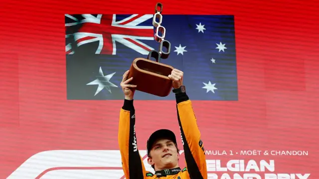 Oscar Piastri holds the winners trophy at Spa aloft on the podium.