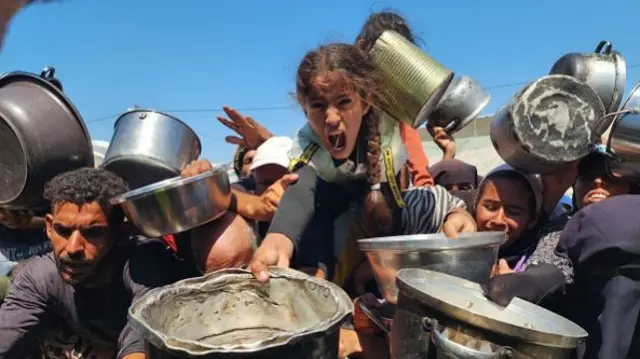 Palestinians struggling with hunger crowd around as a charity distributes food in the Al-Mawasi area of Khan Yunis