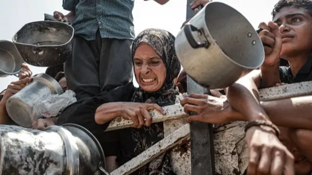 Palestinians wait in queue to get hot meals distributed by aid organizations in Gaza City,