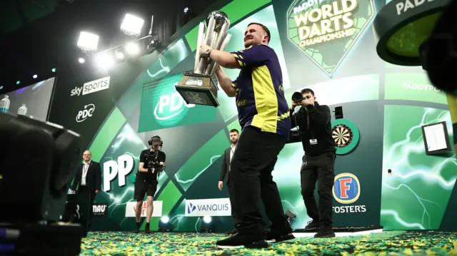 Luke Littler holds the World Championship trophy