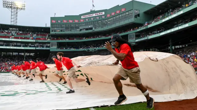 Grounds crew members remove the tarp from the infield before a game