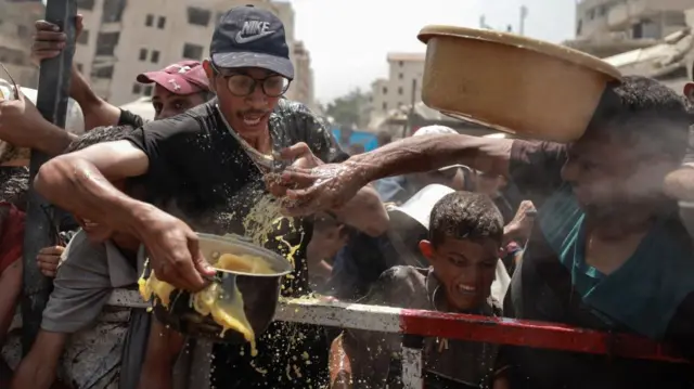 Palestinians react as they gather to receive food from a charity kitchen