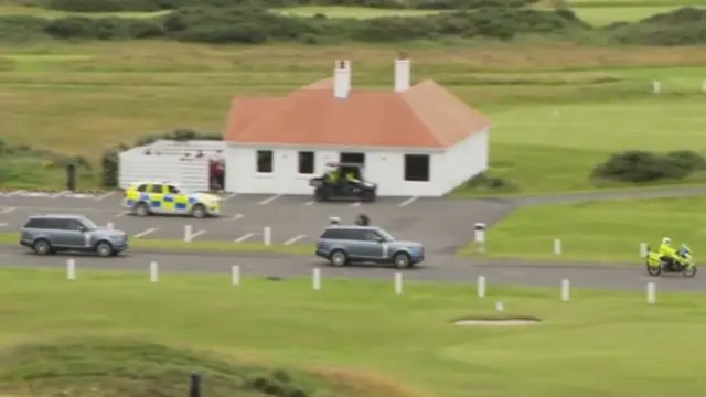 Two range rovers driving in front of golf course escorted by police