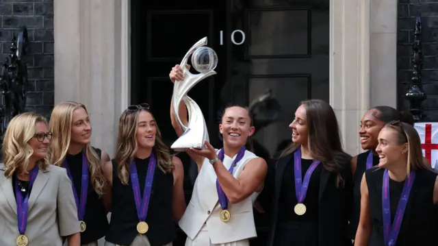 England's Maya Le Tissier holds the trophy next to manager Sarina Wiegman and teammates