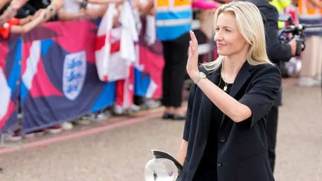 England's defender Leah Williamson waves to fans waiting with banners and flags to welcome the England Women's national football team