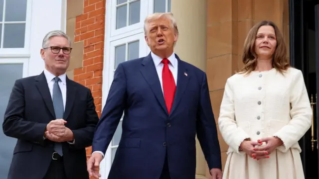 Trump in between Starmer and Starmer's wife as he speaks holding his hands out to his sides